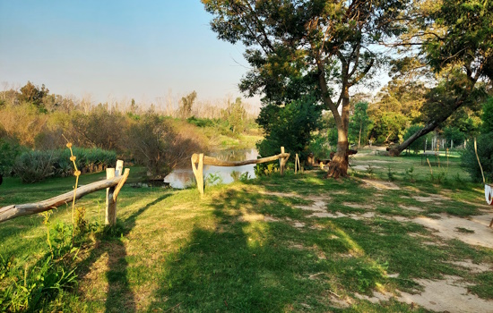 Pole fence between campsite and grass terrace below next to river.